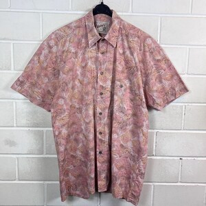 Könnte beinhalten: Ein kurzärmeliges Hemd mit Knopfleiste in einem abstrakten Blattmuster in gedecktem Rosa und Beige. Das Hemd verfügt über einen klassischen Kragen, eine durchgehende Knopfleiste und eine Brusttasche auf der linken Seite. Das Etikett zeigt Wafer's.