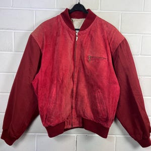 Könnte beinhalten: Rote Vintage-Bomberjacke mit Reißverschluss und kleiner Brusttasche. Die Jacke hat einen gerippten Kragen, Bündchen und Saum. Die Ärmel sind dunkler rot als der Körper der Jacke.