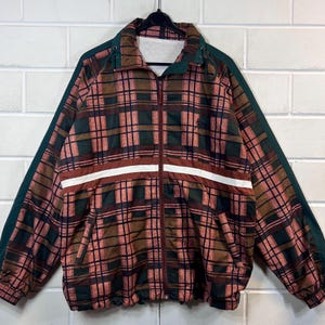 Peut inclure: Une veste en tissu à carreaux vert et marron avec une fermeture éclair. La veste a une bande blanche sur la poitrine et un petit logo sur le côté droit.