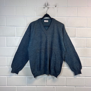 May include: A dark blue v-neck sweater hanging on a black hanger against a white brick wall.