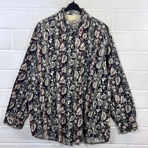 Könnte beinhalten: Ein langärmliges Hemd mit Knöpfen, floralem Muster und vertikalen Streifen. Das Hemd ist aus leichtem Stoff und hat eine lockere Passform. Das Etikett auf dem Hemd lautet "Shirting Olive".