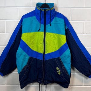 May include: A blue, green and black colour block jacket with a zip closure. The jacket has a high collar and a drawstring at the bottom.