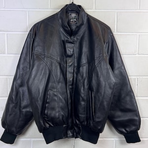 Peut inclure: Veste en cuir noir avec col montant, fermeture éclair sur le devant et deux poches latérales. La veste a un ourlet et des poignets en tricot côtelé. La marque "Berlin" est visible sur un petit patch près du col.