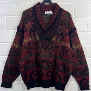 May include: A vintage burgundy sweater with a geometric pattern in black, green, and gold. The sweater has a shawl collar and black trim on the cuffs and hem. The label reads "Cote d'Azur".