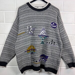 May include: A vintage patterned sweater in black, white, and grey. The sweater has a crew neck and long sleeves with black cuffs and hem. It features colourful abstract shapes in purple, blue, and yellow.