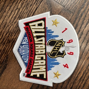 Op de afbeelding: Geborduurde patch met de tekst "ALLSTAR GAME" en "1994", plus het NHL-logo. De patch bevat ook "Madison Square Garden" en "New York City". Het ontwerp heeft een witte achtergrond met rode, blauwe en gouden details.