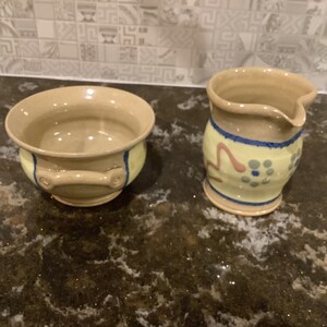 May include: A set of two handmade ceramic bowls, one with a blue and yellow design and the other with a simple brown glaze. The bowls are ideal for serving sugar and creamer.