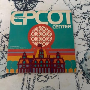 Può includere: Un libretto souvenir quadrato vintage dell'EPCOT Center con il logo Walt Disney World, una grande sfera geodetica rossa e un'illustrazione stilizzata di un edificio. Il testo recita EPCOT CENTER e Compliments of Eastman Kodak Company.