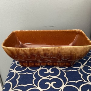 May include: A rectangular brown ceramic planter with a glazed finish and a swirl pattern. The planter has a slightly rounded bottom and a squared top.