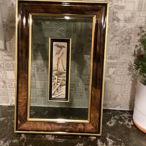 May include: A framed silver relief sculpture depicting a sailboat with a bird flying overhead. The frame is made of dark wood with gold accents.