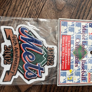 May include: A Mets 40th Anniversary 2002 patch with the text "1962" and "Major League Baseball Collectibles" on the tag. The patch is in a plastic sleeve and has a brown, blue, green, and white color scheme.