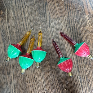 May include: Five vintage-style Christmas light bulbs with metallic screw bases. Three bulbs feature yellow glass tips with green fluted plastic bases, while two bulbs have red glass tips with red fluted plastic bases, all arranged in a loose cluster.