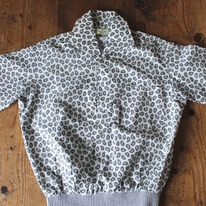 Può includere: Una camicia bianca a maniche corte con motivo paisley e fascia elastica blu e bianca.