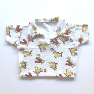May include: White collared shirt featuring a pattern of red and yellow squirrels holding branches. The shirt has short sleeves and a classic collar. The fabric appears to be a soft, absorbent material.