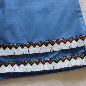 May include: A blue fabric with a white fringe trim and a red, green, and black geometric pattern.