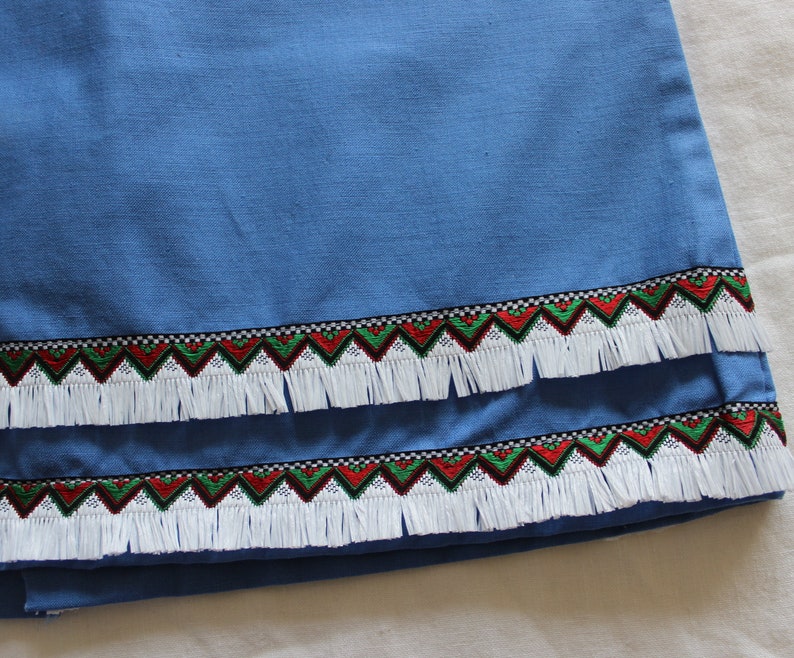 May include: A blue fabric with a white fringe trim and a red, green, and black geometric pattern.