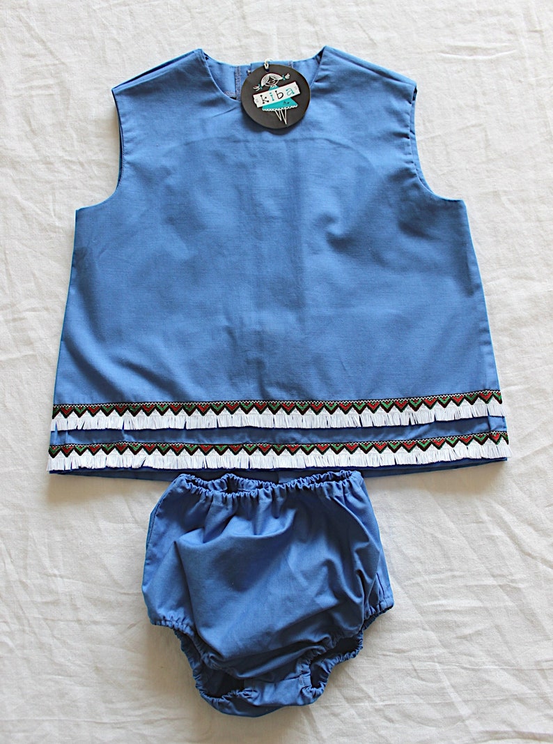 May include: A blue sleeveless top with a white and red trim and a matching blue diaper with a ruffled edge. The top has a tag that says "Kiba".