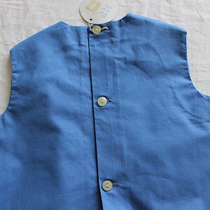 May include: A sleeveless blue cotton vest with three white buttons down the back.
