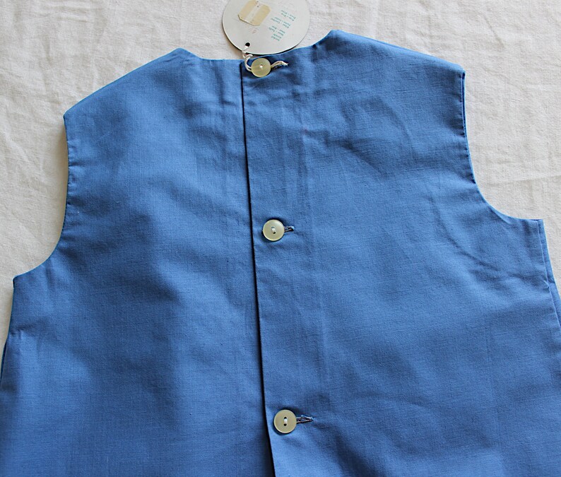 May include: A sleeveless blue cotton vest with three white buttons down the back.