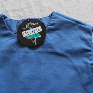 May include: A sleeveless blue shirt with a black and white label that says "kiba" and features a cartoon girl wearing a dress.