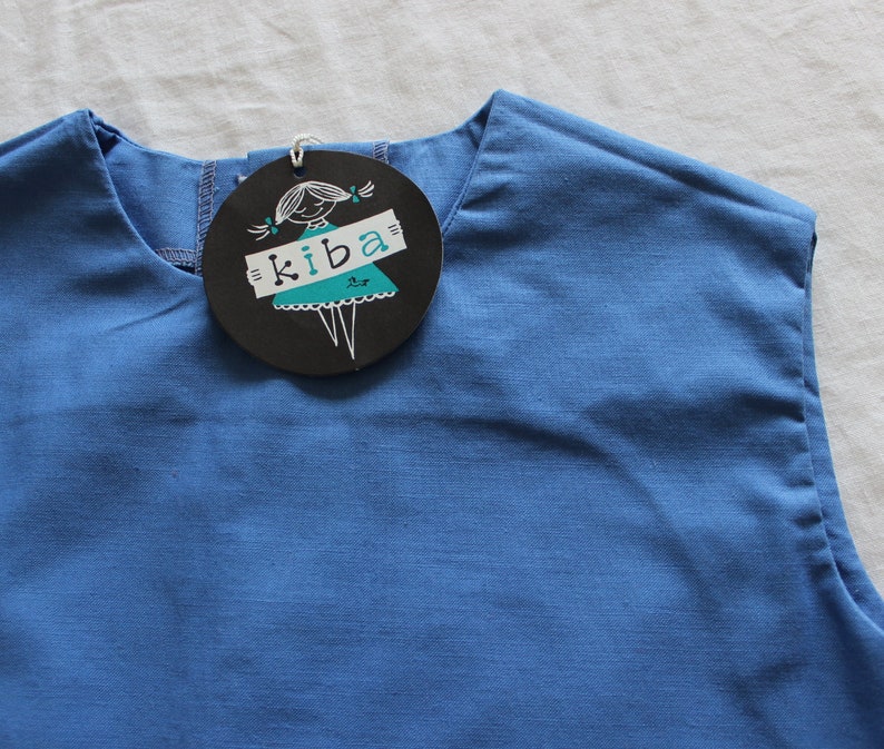 May include: A sleeveless blue shirt with a black and white label that says "kiba" and features a cartoon girl wearing a dress.