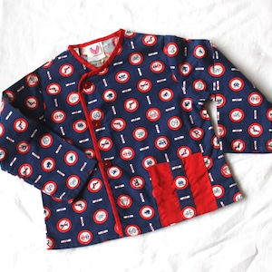 May include: Navy blue jacket with a red trim and pocket. The jacket features a pattern of red and white road signs on a navy background. It has red buttons and a red collar.