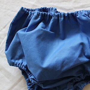 May include: A pair of blue baby bloomers with a gathered elastic waistband.
