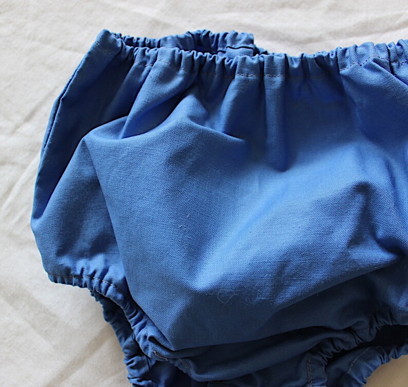 May include: A pair of blue baby bloomers with a gathered elastic waistband.