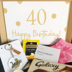 Könnte beinhalten: Eine Geschenkbox gefüllt mit Geburtstagsgeschenken zum 40. Geburtstag. Die Box enthält einen Teebeutel, eine Tafel Schokolade, eine Kerze, einen Schlüsselanhänger, ein Paar Socken und eine Karte. Die Karte lautet: "An Jane, Ich wünsche dir einen wunderschönen Geburtstag. Bis bald zum Prosecco-Trinken! Liebe Grüße von uns allen xxx".