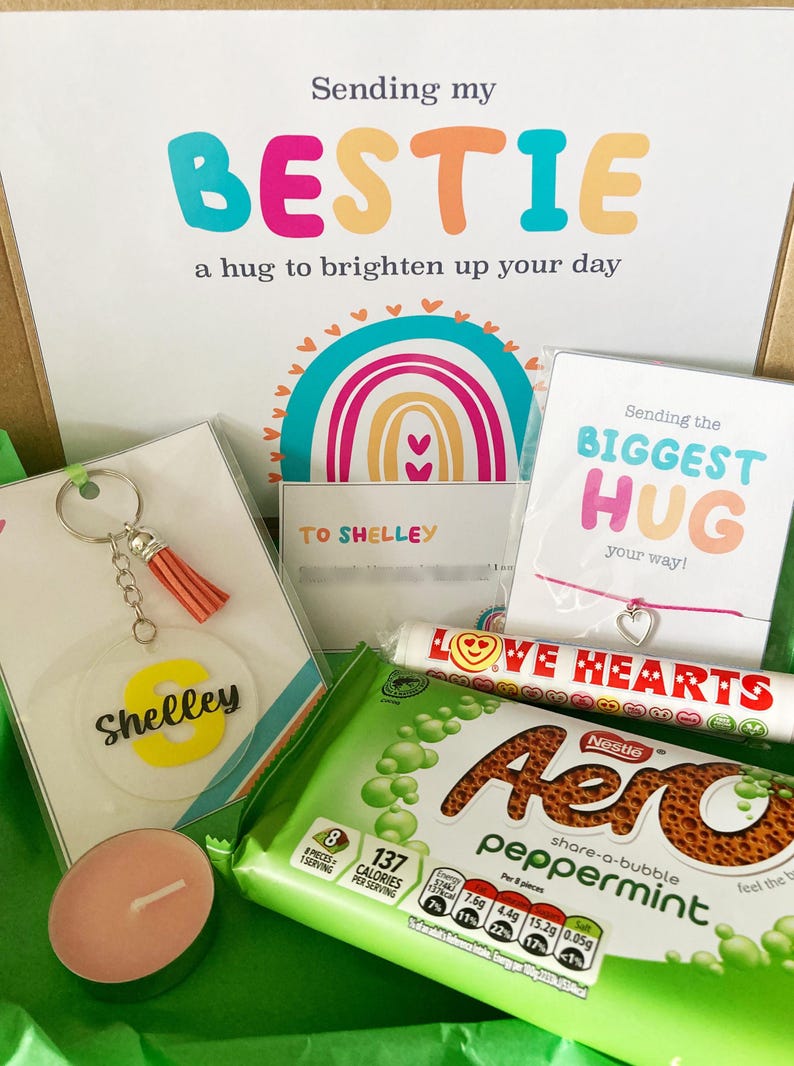 May include: A gift box with a variety of items, including a keychain with a tassel, a candle, a bracelet, and a candy bar. The box also contains a card that says "Sending my BESTIE a hug to brighten up your day."