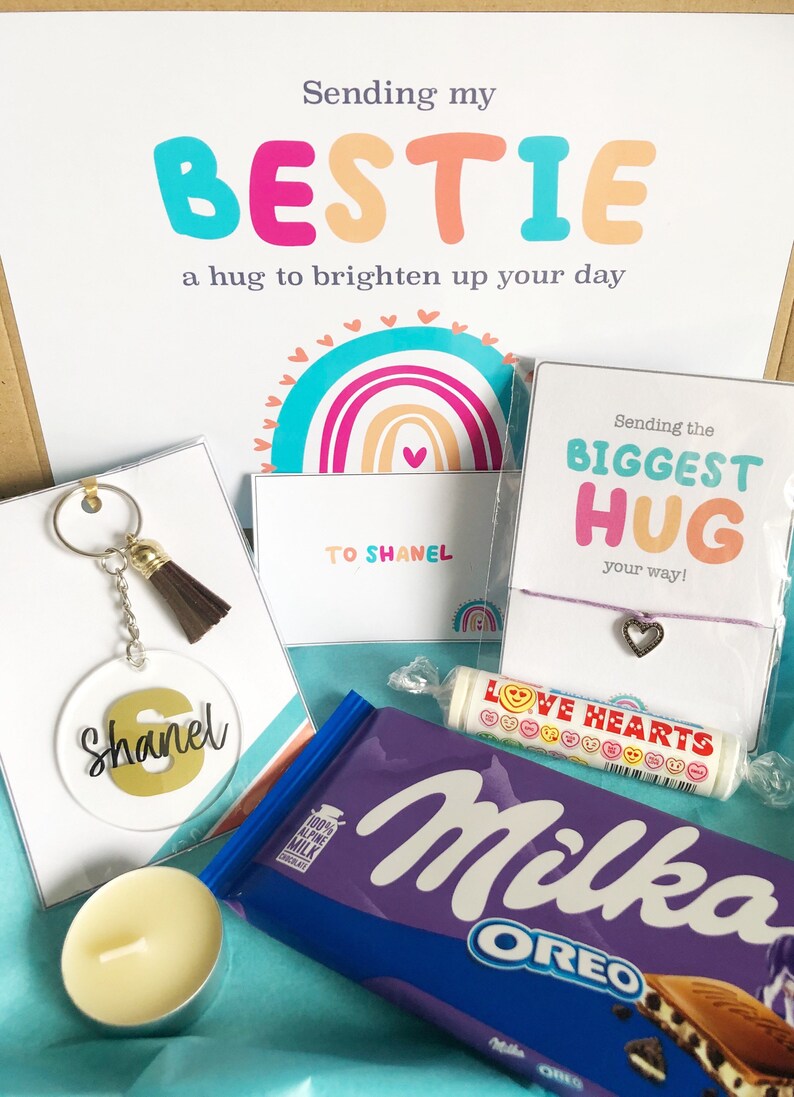 May include: A gift box with a variety of items, including a keychain, a bracelet, a chocolate bar, a candle, and a candy roll. The box has a card that says "Sending my BESTIE a hug to brighten up your day". The keychain has the name "Shanel".