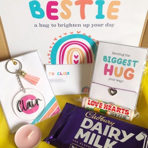 May include: A gift box with a variety of items, including a keychain, bracelet, candy, chocolate bar, and a candle. The box contains a card that says "Sending my BESTIE a hug to brighten up your day". The keychain has a pink tassel.