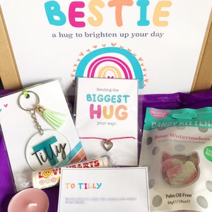 May include: A gift box filled with treats and a personalized message. The box includes a keychain, a bracelet, a candle, a bag of candy, and a card that says "Sending my BESTIE a hug to brighten up your day."