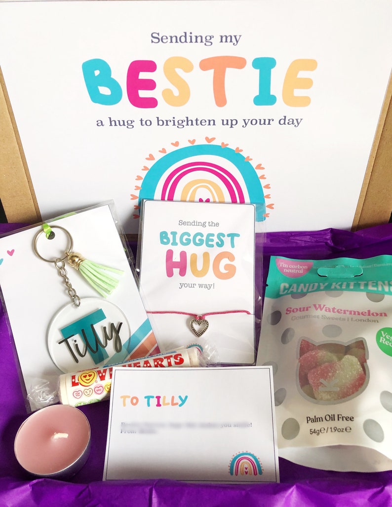 May include: A gift box filled with treats and a personalized message. The box includes a keychain, a bracelet, a candle, a bag of candy, and a card that says "Sending my BESTIE a hug to brighten up your day."