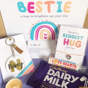 May include: A gift box with a variety of items, including a keychain with the name "Nevey", a chocolate bar, a candle, and a card that says "Sending my BESTIE". The box also contains a bracelet and a candy roll.