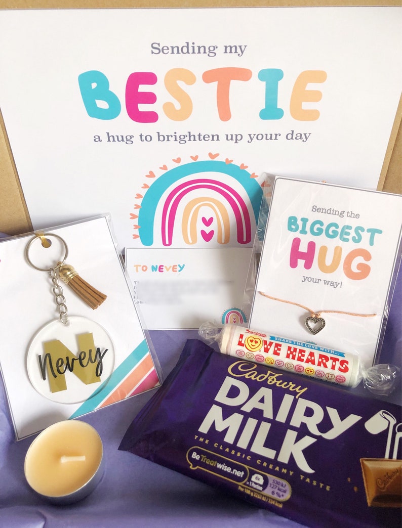 May include: A gift box with a variety of items, including a keychain with the name "Nevey", a chocolate bar, a candle, and a card that says "Sending my BESTIE". The box also contains a bracelet and a candy roll.