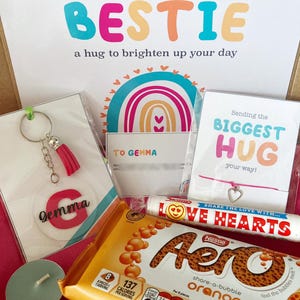 May include: A gift box with a variety of items. Includes a keychain with a pink tassel and the name "Gemma", a chocolate bar, a bracelet, and cards with the phrases "Sending my BESTIE" and "Sending the BIGGEST HUG".