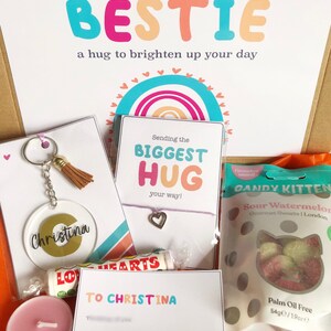 May include: A gift box with a variety of items, including a keychain, bracelet, lip balm, candle, and sweets. The box includes cards with the phrases "Sending my BESTIE" and "Sending the BIGGEST HUG." The keychain has the name "Christina."