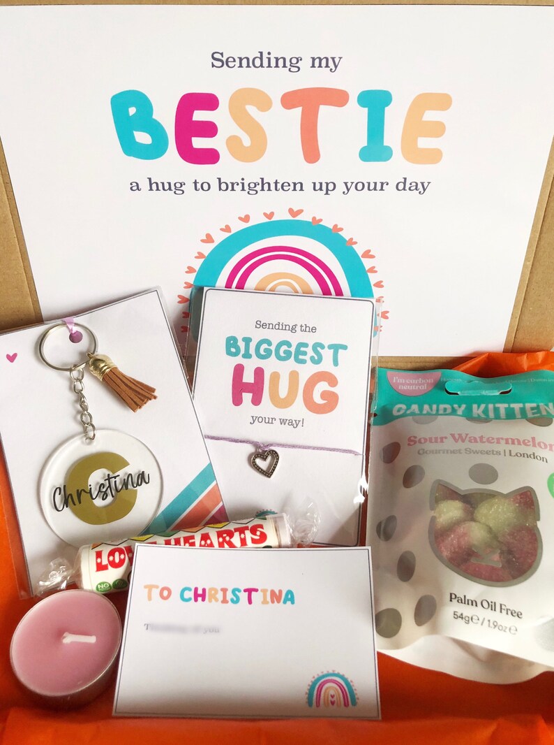 May include: A gift box with a variety of items, including a keychain, bracelet, lip balm, candle, and sweets. The box includes cards with the phrases "Sending my BESTIE" and "Sending the BIGGEST HUG." The keychain has the name "Christina."