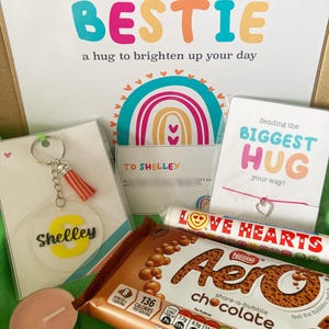 May include: A gift box with a card that says "Sending my BESTIE a hug to brighten up your day." Includes a keychain, a bracelet, a chocolate bar, a candle, and a candy roll. The keychain has a tassel and the name "Shelley".