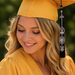 May include: A smiling person wearing a yellow graduation cap and gown. The cap has a black tassel with a charm featuring two oval portraits and the year 2026. The image is from Crafting Boutique.