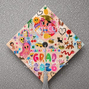 May include: A decorated graduation cap with a variety of colorful illustrations. The design includes a mermaid, rainbow, sun, and the words "MAÑANA SERA BONITA" and "GRAD 2020". A gray tassel hangs from the center.