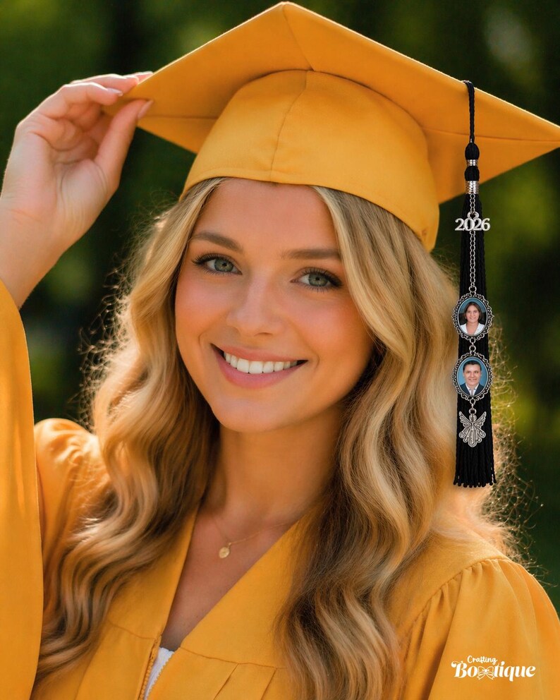 May include: A smiling person wearing a yellow graduation cap and gown. The cap has a black tassel with a 2026 charm and two photo charms. The gown is a matching yellow color. The image is taken outdoors.
