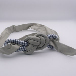 May include: A gray fabric belt with a knotted design. The knot is made of a striped fabric with blue and white stripes.