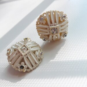 May include: A pair of white, round, ornate earrings with clear rhinestone accents.