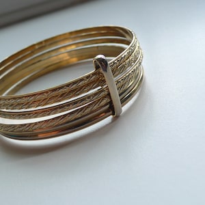 May include: A set of four gold-toned bangle bracelets with a textured design. The bracelets are stacked on top of each other.