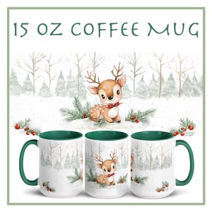 May include: A white ceramic coffee mug with a green rim. The mug features a watercolor illustration of a fawn in a snowy forest. The text "15 oz COFFEE MUG" is printed at the top of the mug.