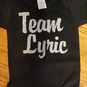 May include: Black bodysuit with silver glitter lettering that reads "Team Lyric".