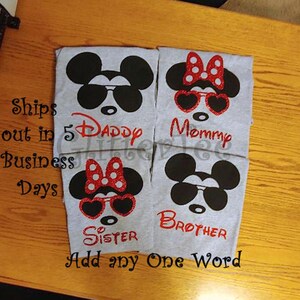 K&ouml;nnte beinhalten: Vier graue T-Shirts mit einem schwarz-wei&szlig;en Mickey-Mouse-Motiv. Jedes Shirt hat eine rote Schleife und eine Sonnenbrille. Die Shirts sind mit "Daddy", "Mommy", "Sister" und "Brother" beschriftet.
