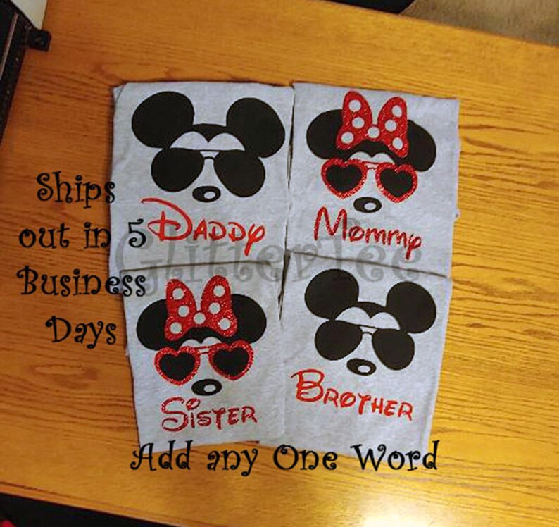 K&ouml;nnte beinhalten: Vier graue T-Shirts mit einem schwarz-wei&szlig;en Mickey-Mouse-Motiv. Jedes Shirt hat eine rote Schleife und eine Sonnenbrille. Die Shirts sind mit "Daddy", "Mommy", "Sister" und "Brother" beschriftet.